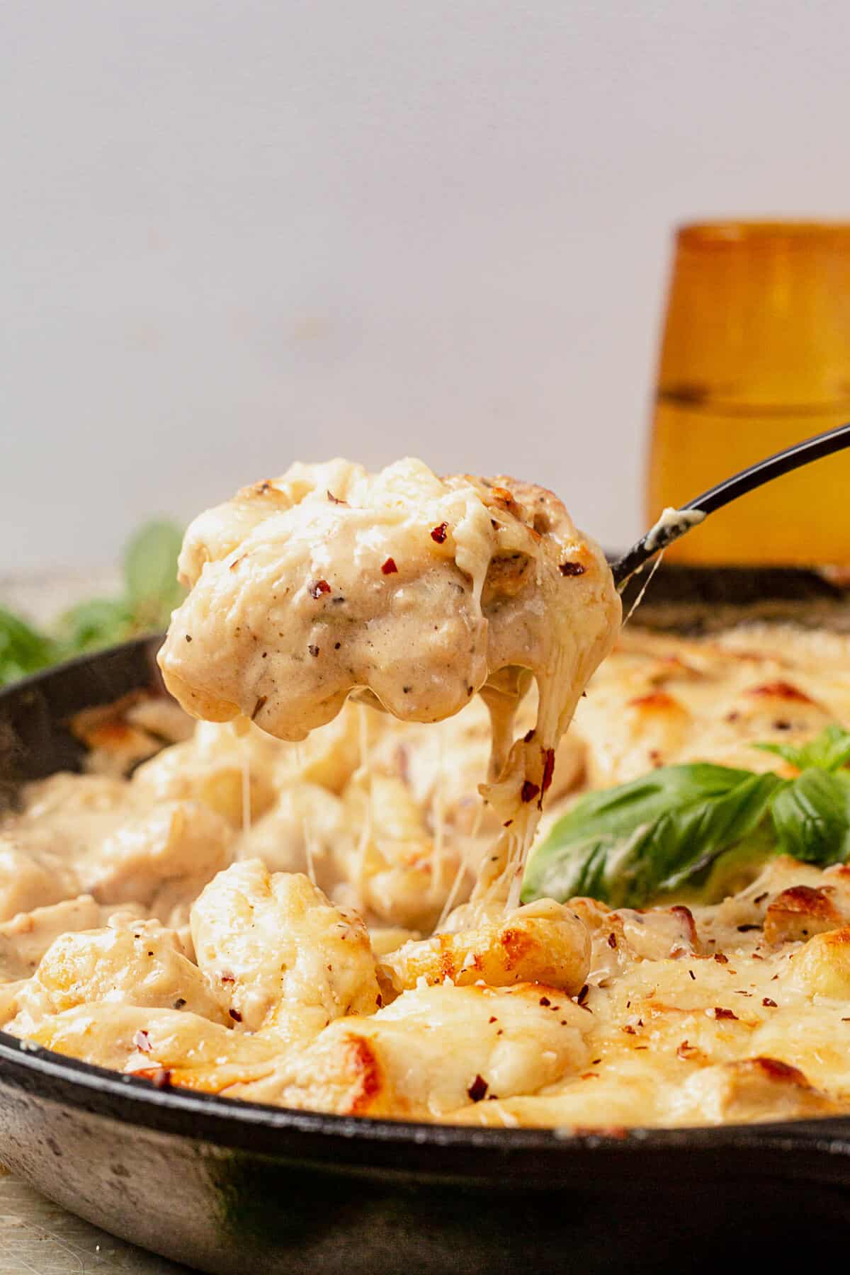 scooping chicken alfredo gnocchi out of a skillet